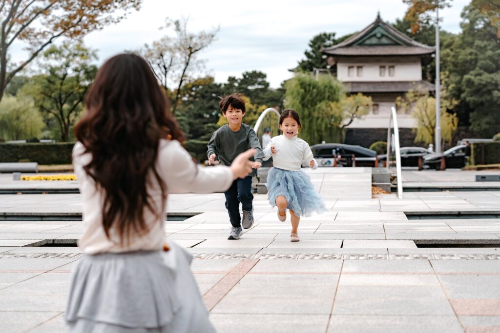皇居の櫓を背に、両手を広げる母親のもとへ駆け寄るふたりの子ども